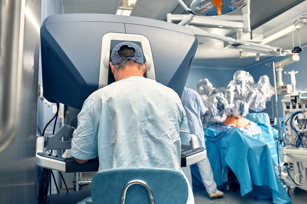 A surgeon operates a robotic surgical system in an operating room, with a medical team and patient visible in the background.